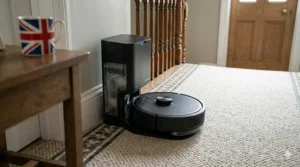 A docked robot vacuum with mapping and self-emptying base shown next to a Union Jack mug on a dark oak side table.