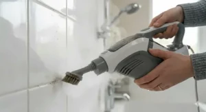Close-up of a handheld steam cleaner attachment sanitising white bathroom tiles with high-pressure steam.