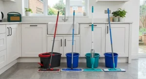 A microfibre flat floor mop cleaning dried muddy footprints and paw prints from a grey tiled kitchen floor with a fine spray mist.