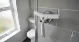 A modern shower squeegee hanging from a clear suction cup hook inside a wet room.