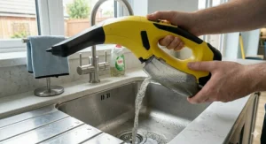 User emptying the dirty water tank of a cordless window vacuum into a kitchen sink.