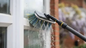 Water fed pole brush with integrated rinse bar spraying pure water onto a window.