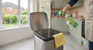 Wiping down the rubber seal and lid rim of a modern sensor kitchen bin with an antibacterial spray.