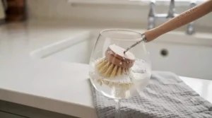 Washing-up brush drying upright in a ceramic sink caddy alongside a dishcloth.