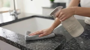 Person wiping down a glossy quartz and granite kitchen island with a daily kitchen spray for granite worktops.