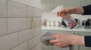 Wiping down kitchen tiles and the splashback using a grease-cutting cleaning spray.